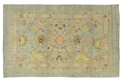 A rectangular vintage area rug with a faded sage green background and an intricate central floral medallion pattern in muted yellow, pink, and brown tones.