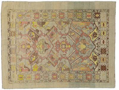 An vintage-style rectangular area rug with a faded medallion and geometric pattern in muted tones of beige, dusty blue, pink, yellow, and brown.