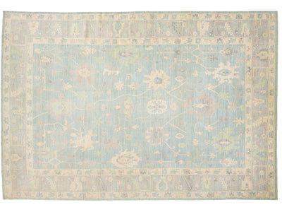 An oushak-style rectangular area rug with a traditional floral pattern, featuring a light blue center field surrounded by beige and muted green borders.