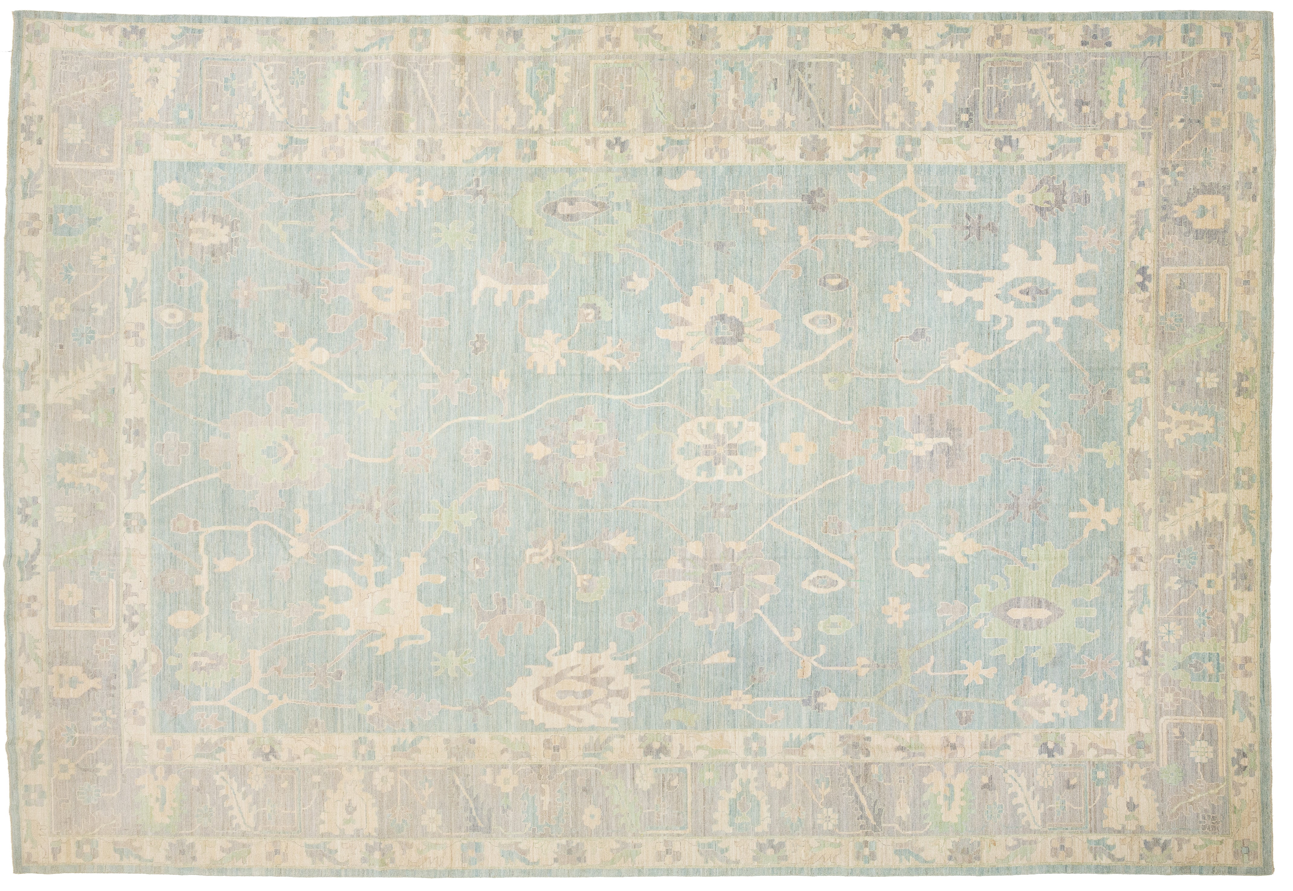 An oushak-style rectangular area rug with a traditional floral pattern, featuring a light blue center field surrounded by beige and muted green borders.