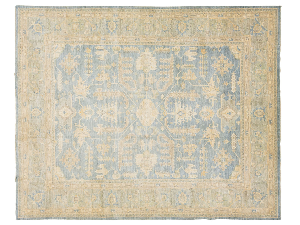 An oushak-style rectangular area rug with a traditional pattern, featuring a dusty blue central field and a warm beige border.