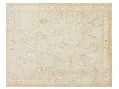 A rectangular area rug with a traditional pattern in muted pastel tones of sage green, beige, and light gray.