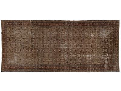 A rectangular vintage-style area rug with an intricate, distressed geometric pattern in shades of brown, beige, and muted red, shown flat against a white background.