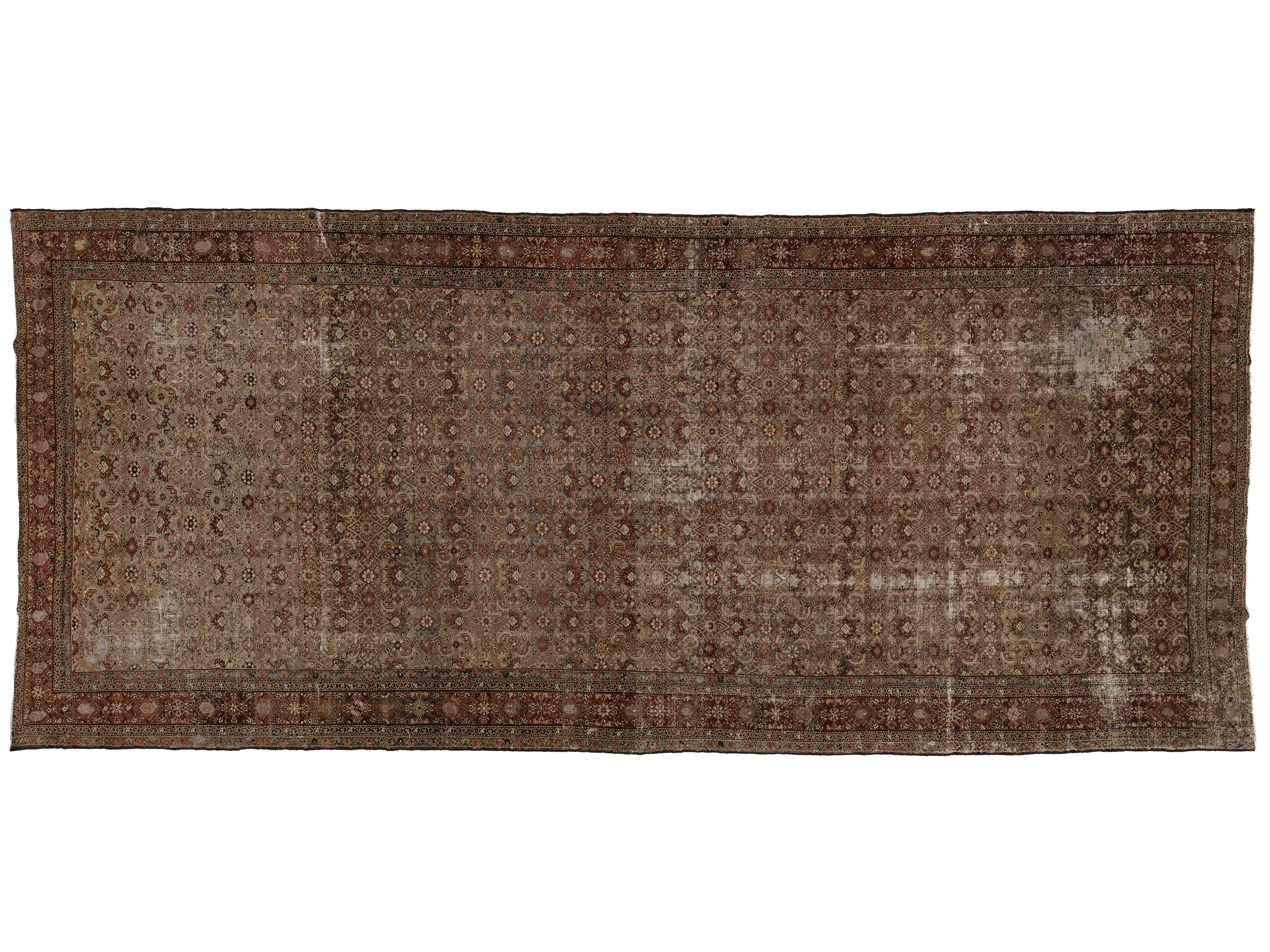 A rectangular vintage-style area rug with an intricate, distressed geometric pattern in shades of brown, beige, and muted red, shown flat against a white background.