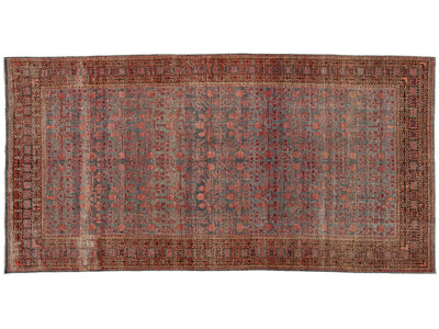 A rectangular antique area rug with an intricate floral and geometric pattern in muted red, rust, gray, and brown tones, featuring a detailed border.