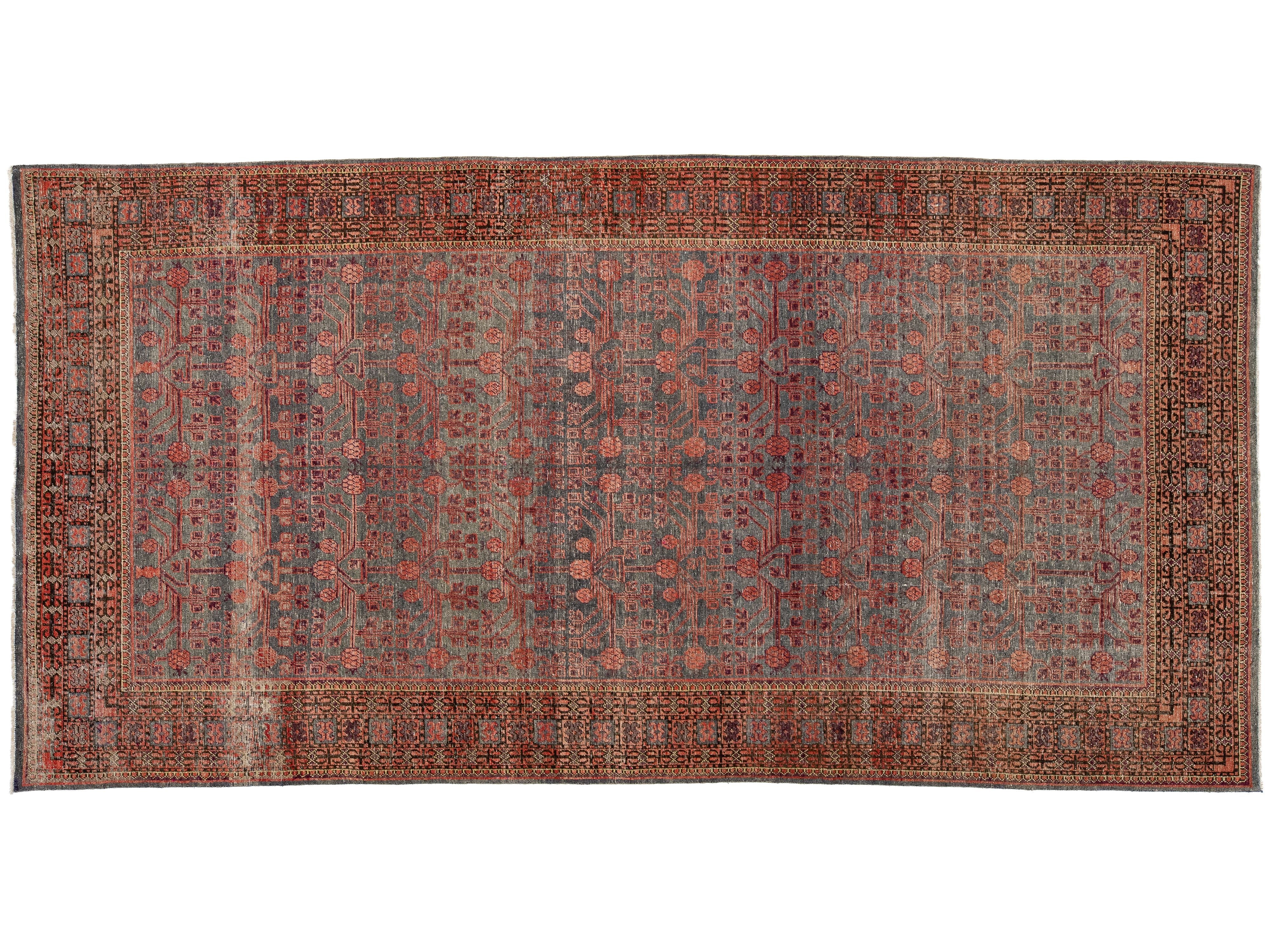 A rectangular antique area rug with an intricate floral and geometric pattern in muted red, rust, gray, and brown tones, featuring a detailed border.