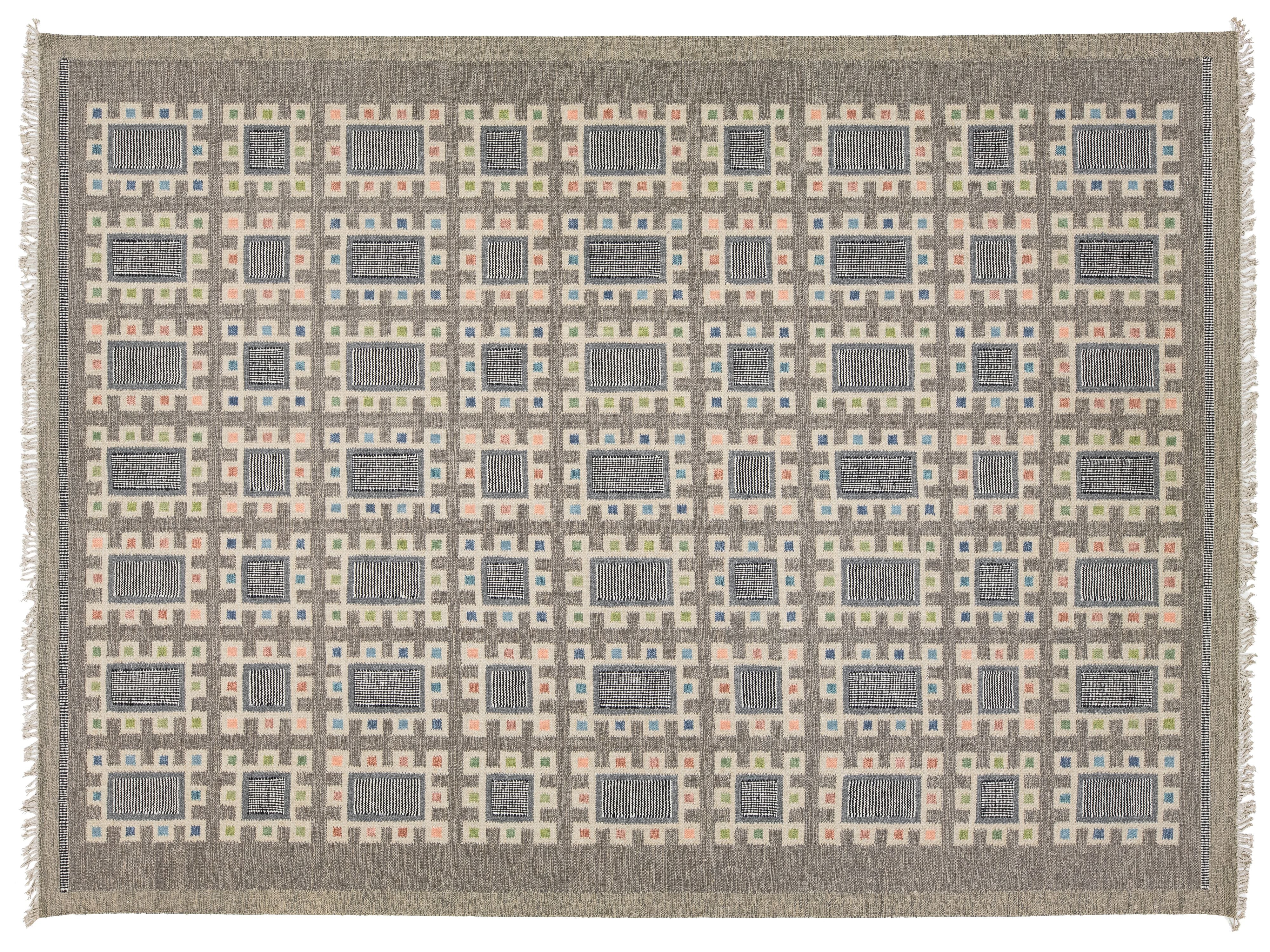 A rectangular area rug with a geometric grid pattern in shades of gray, beige, and muted peach, finished with white fringe on the sides.