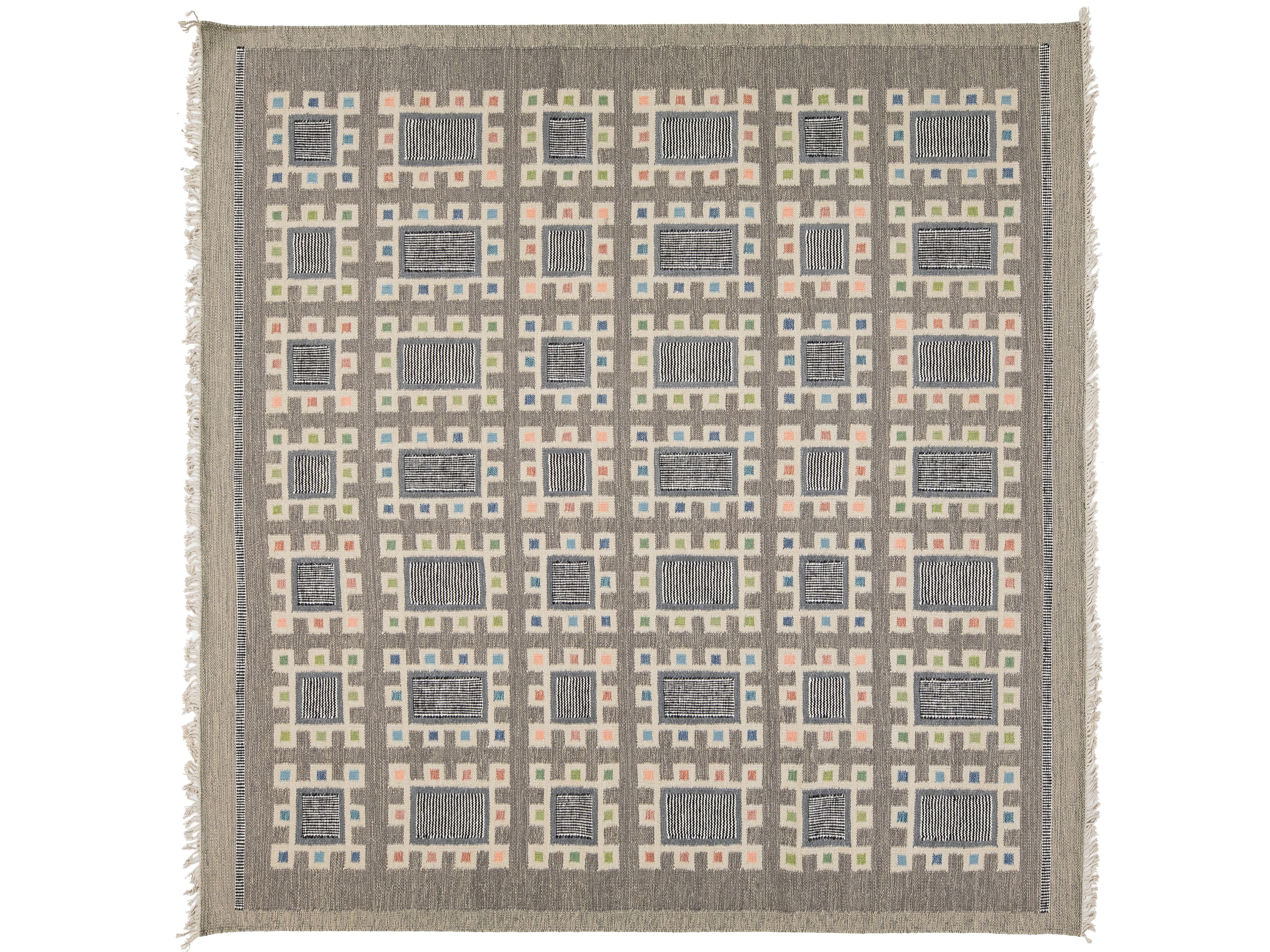A square woven area rug with a geometric grid pattern in taupe, slate blue, blush pink, and pale yellow, finished with fringed edges.
