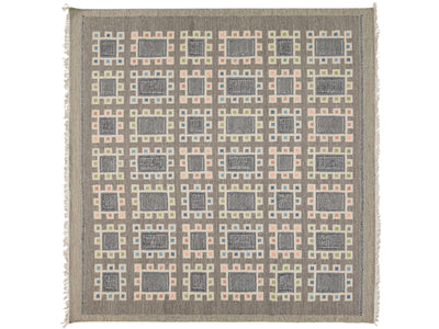 A square woven area rug with a geometric grid pattern in taupe, slate blue, blush pink, and pale yellow, finished with fringed edges.