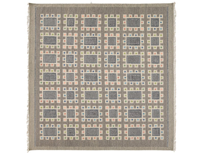A square woven throw blanket with fringe on all sides, featuring a geometric pattern of gray rectangles and small pastel squares in pink, blue, and green on a taupe background.